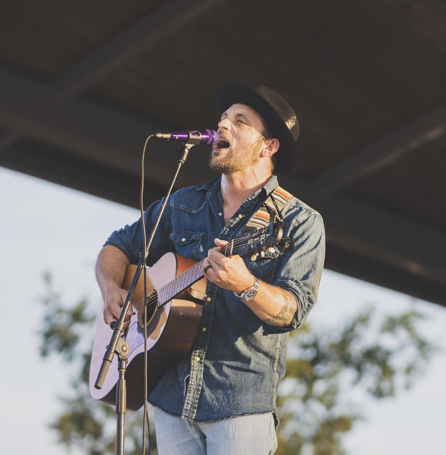 Kevin Holdson singing and playing acoustic guitar on stage